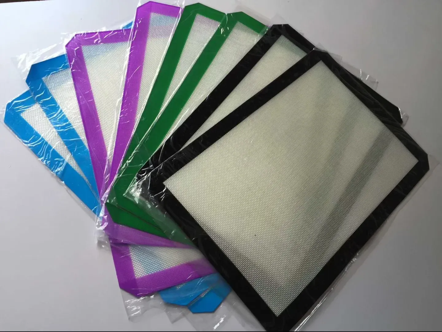 Silicone fiberglass baking mat samples with blue, purple, green and black sealed borders in individual bags