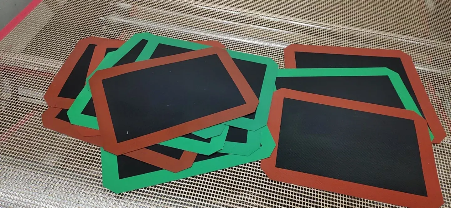 Black open-mesh baking mat samples with green and brown silicone borders and cut corners