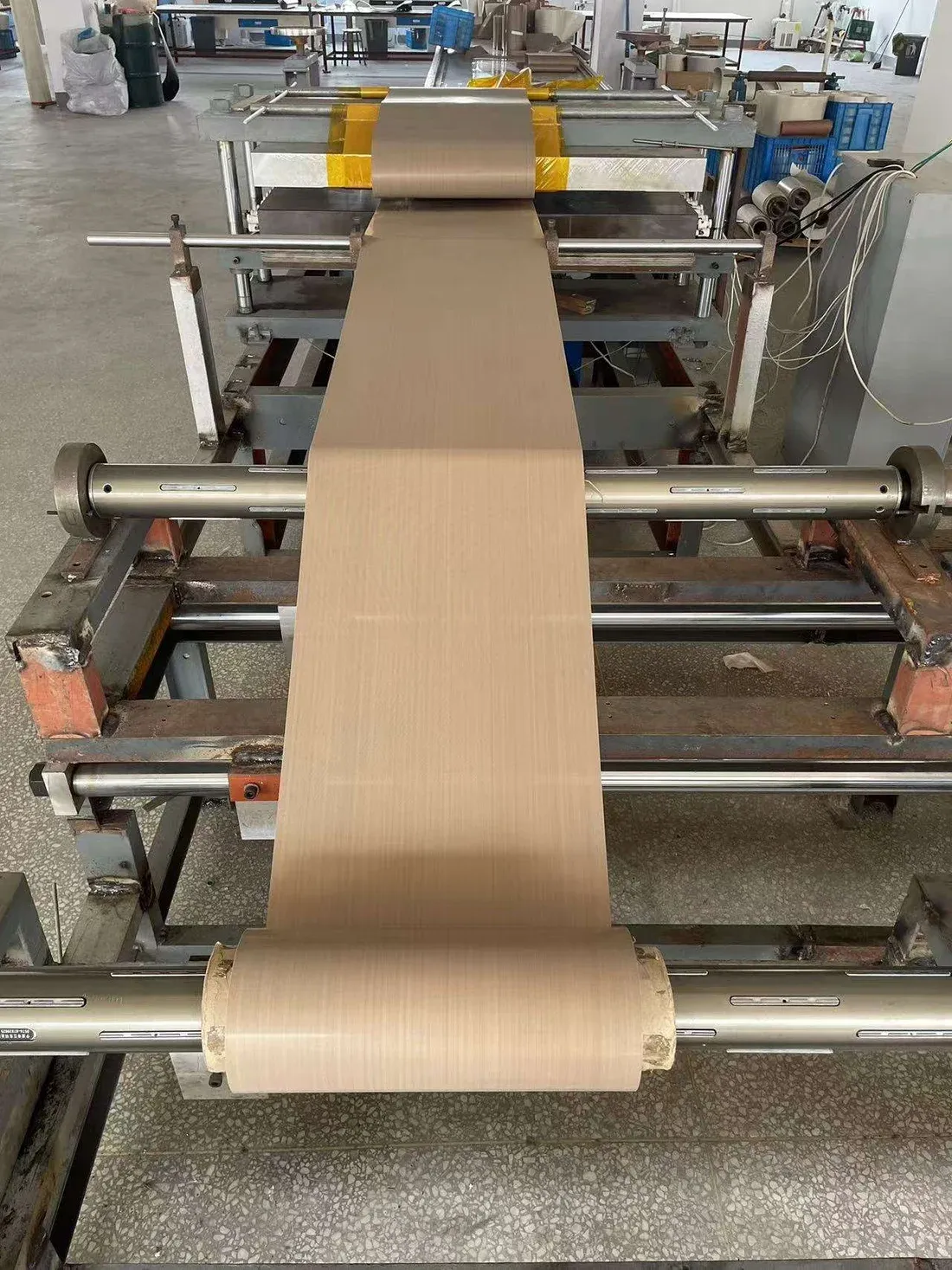 Brown PTFE fabric feeding through roller equipment in a converting workshop