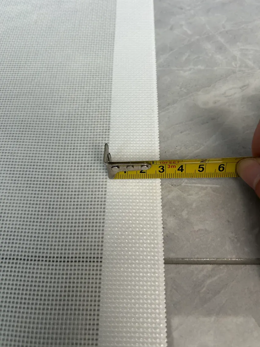 Tape measure checking the sealed white silicone border beside the open fiberglass mesh
