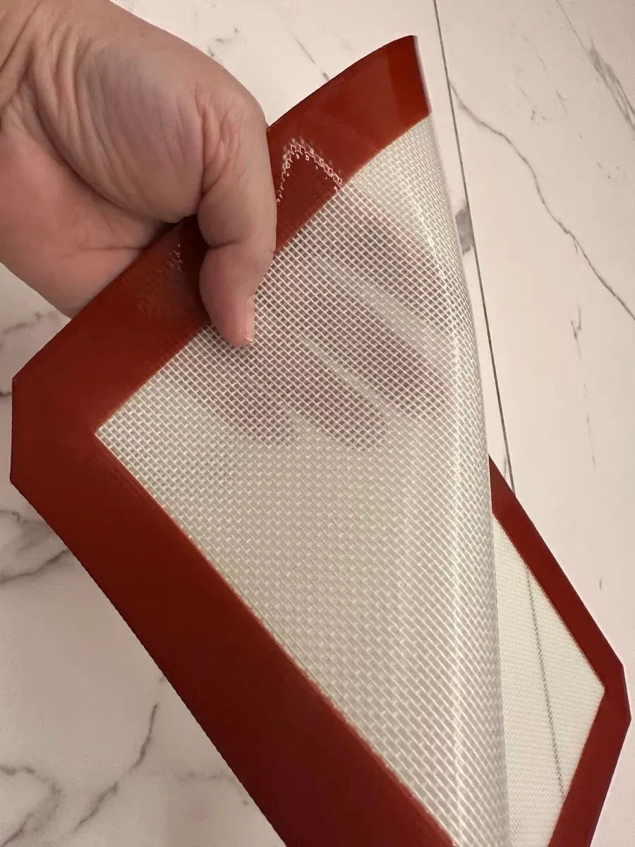 Close-up of a flexible silicone fiberglass baking mat held at its red sealed border
